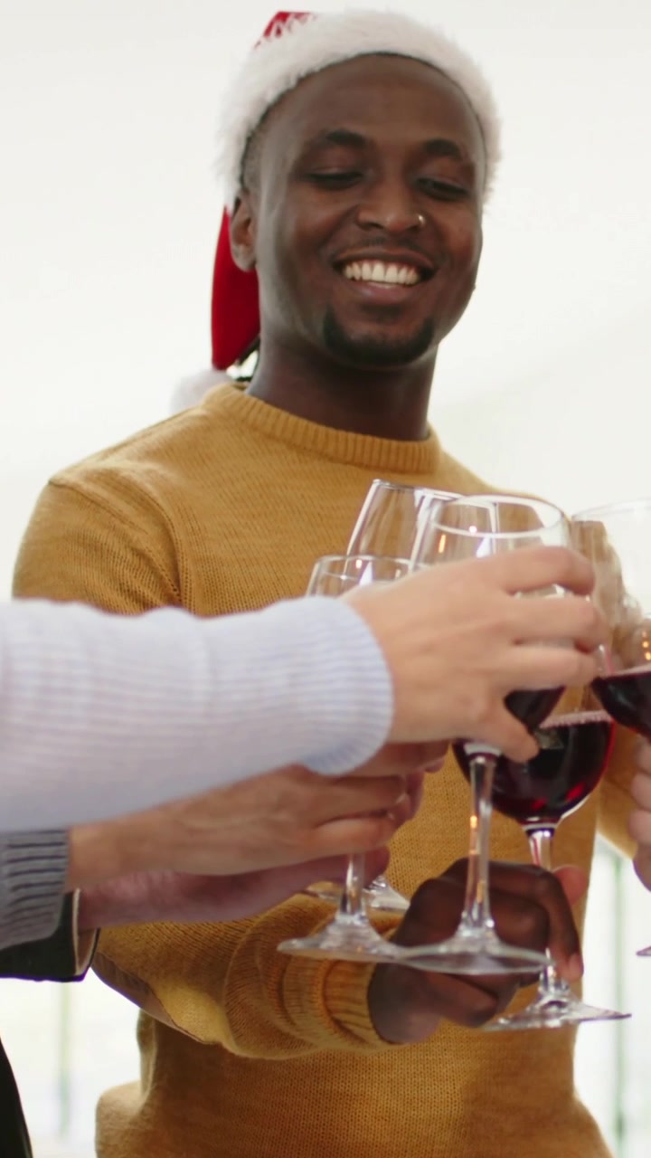 Vertical video: Starting toast, man in mustard sweater, Santa hat clinking wine glasses at home