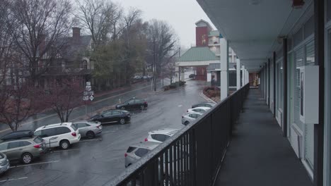 a wide shot of rain pouring down on a covered walkway of a motel that runs parallel to a street with a old victorian house nestled in the background