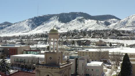 An-aerial-shot-moving-forward-towards-a-small-tower-in-the-middle-of-a-small-town-overlooking-snowy-mountains-in-the-winter