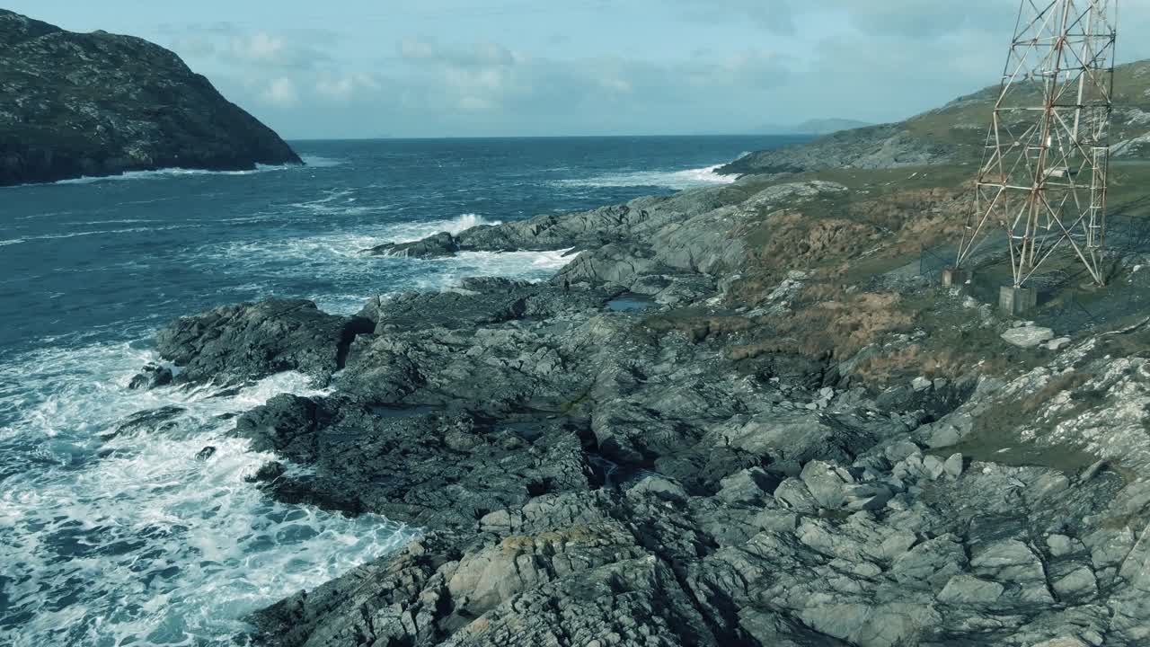 Stationary aerial shot of rocky irish shore line with waves pounding the rocks and coastline during cloudy day