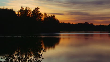 pan right: golden pink cloudy sky at sunset silhouette view from lake