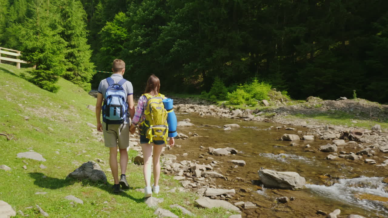 una pareja joven de turistas caminando a lo largo de un río de montaña contra un fondo de viaje forestal verde