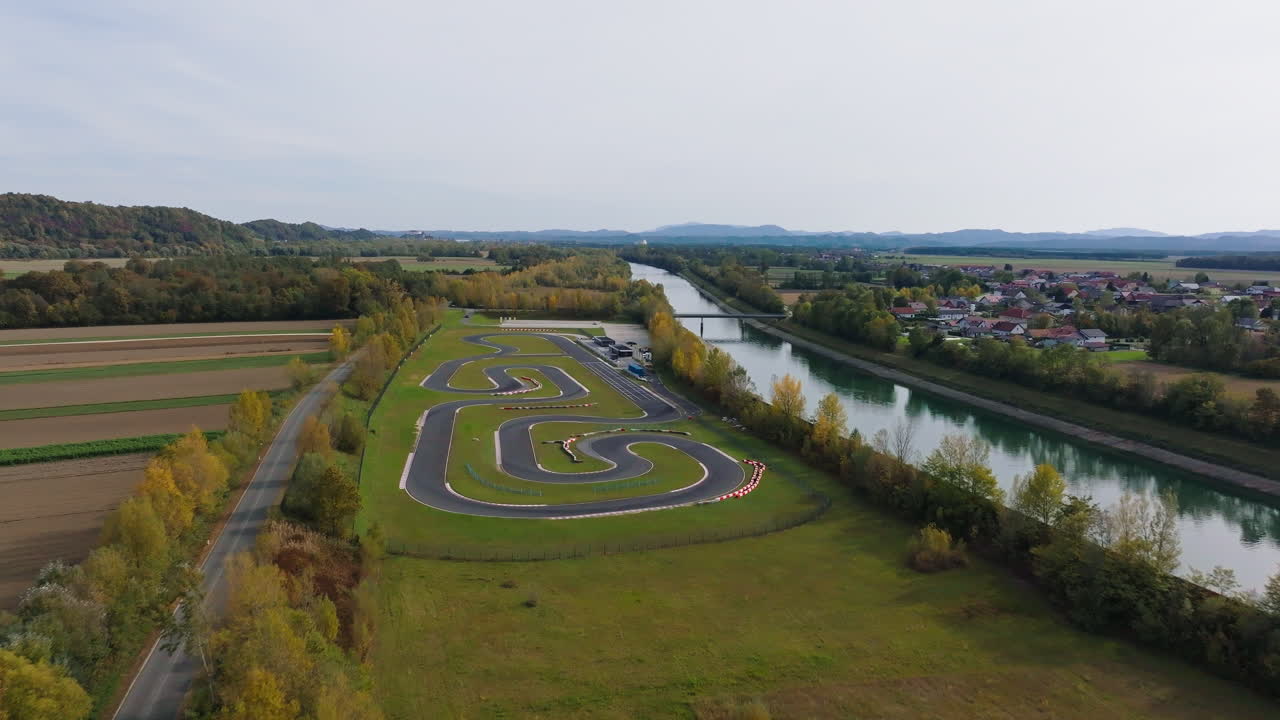 Luftfoto af en gokartbane, der snor sig gennem marker med en nærliggende flod på en klar dag under en