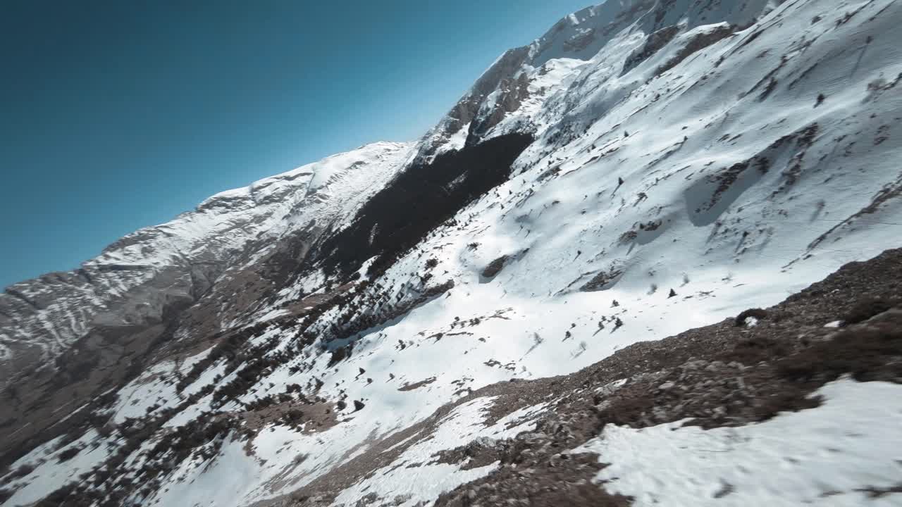 aerial view with fpv drone of a snowy peak mountain then which plunges down from the summit to follow the snowy plateau of the mountain