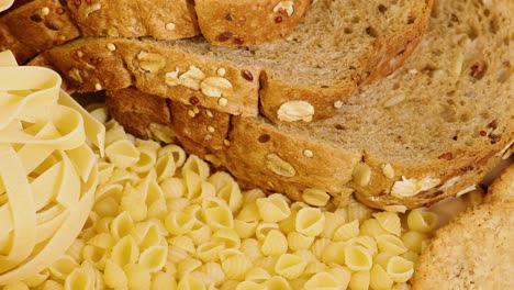 a close-up view of whole wheat bread, pasta, lentils, and corn kernels arranged together under warm lighting