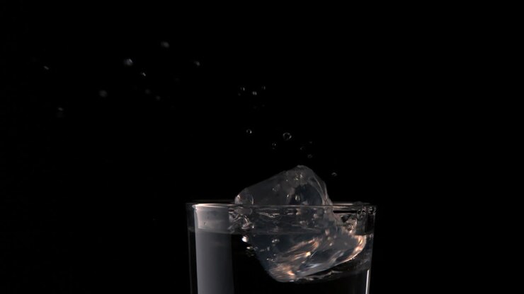 Cubetto di ghiaccio che cade in un bicchiere d'acqua su sfondo nero
