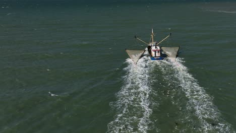 Fishing-trawler-cruising-in-open-ocean-trailed-by-flock-of-seagulls