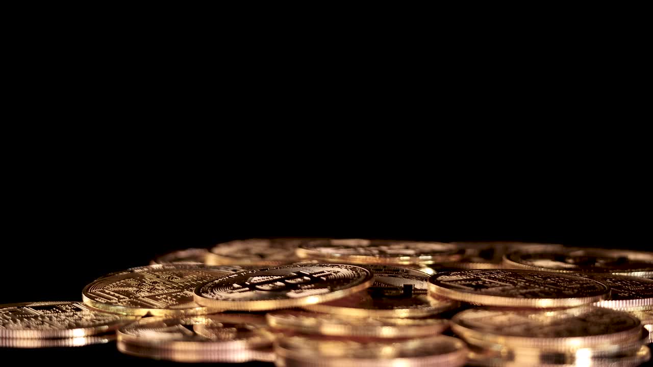 A golden cryptocurrency token drops, bounces, and settles on a pile of coins, dramatic lighting