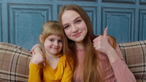 Portrait-of-happy-little-child-kid-daughter-with-young-mother,-hugging,-embracing,-showing-thumbs-up