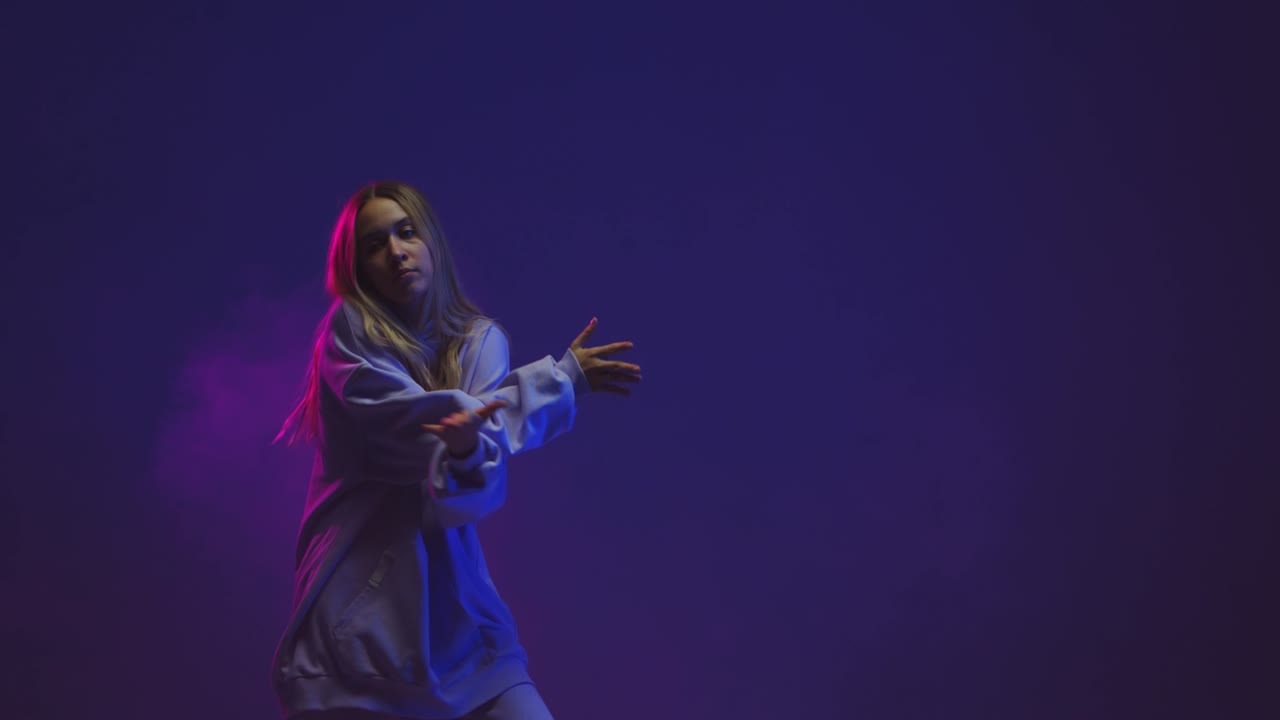 chica adolescente cool bailando hip hop con capucha en luz de neón de colores. video 4k de baile contemporáneo