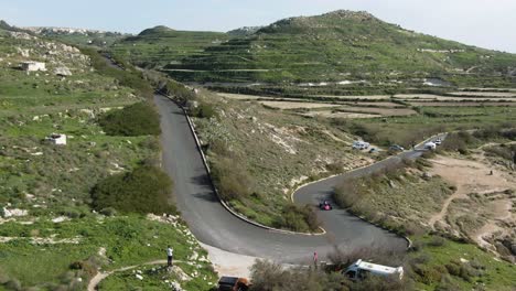pink race car driving on the curved road track on a sunny day - aerial shot