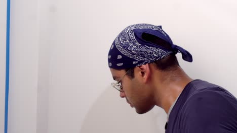 man in head bandana and eyeglasses painting room interior at home