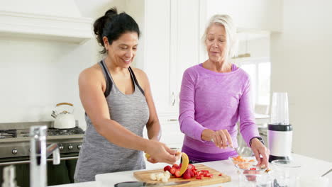 two happy diverse senior women preparing fruits and laughing in sunny kitchen, slow motion