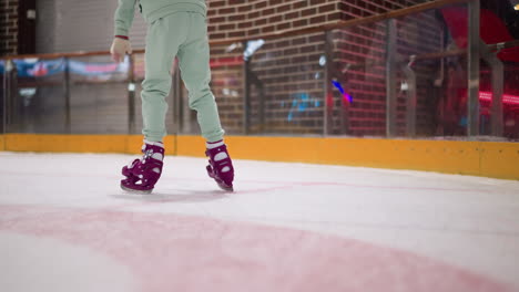 nahaufnahme von jemandem, der in lila eislaufen auf einer eislaufbahn schaitert und aschfarbene hosen und handschuhe trägt