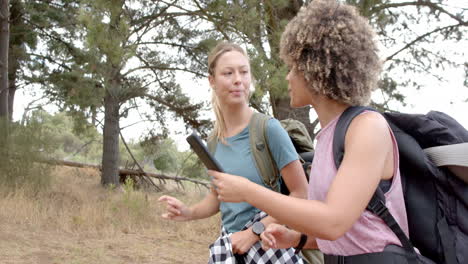 two women are hiking in a wooded area, one holding a smartphone