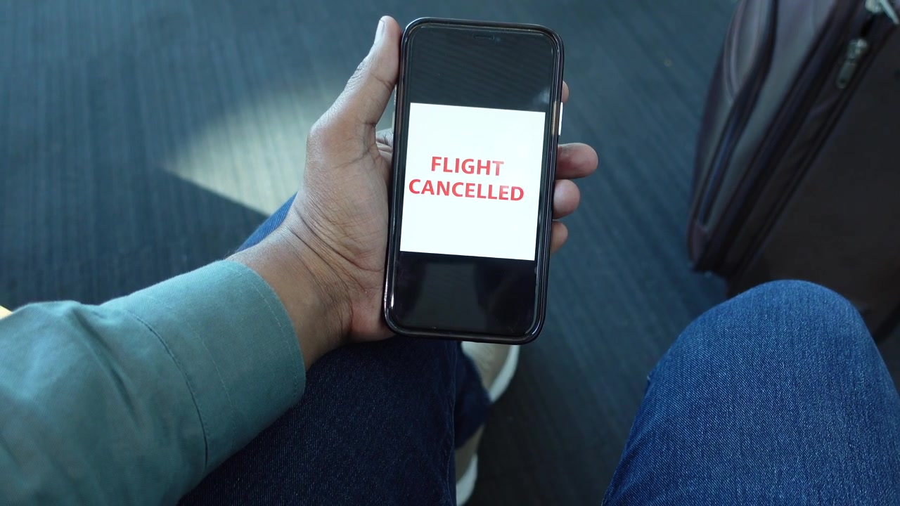 Traveler Holding Smartphone Displaying Flight Cancelled Notification at Airport