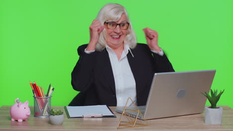 Senior-business-office-woman-analyzes-financial-charts-celebrate-success-win-at-home-workplace-desk