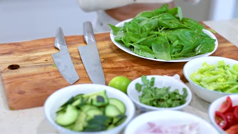hands arranging fresh vegetables and herbs on a wooden board in a bright kitchen setting