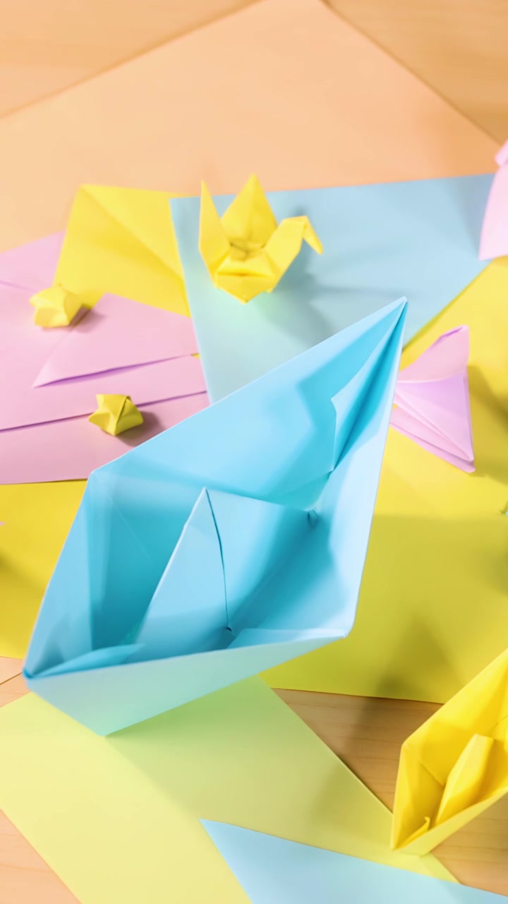 Assorterede origami-dyr og -både arrangeret på pastelpapir, klar belysning, kameraoptagelse ovenfra.