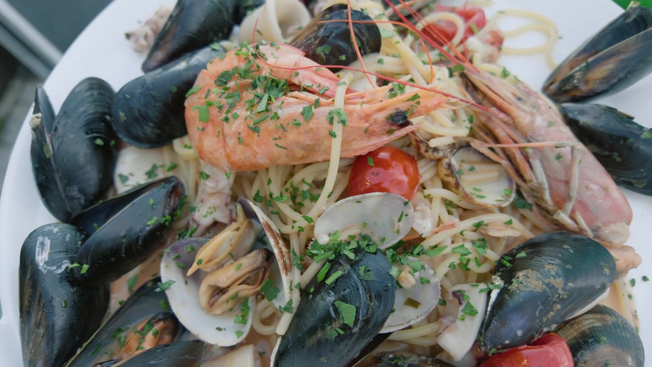 Primo piano di una pasta ai frutti di mare con cozze, vongole, gamberi e pomodorini su un piatto bianco