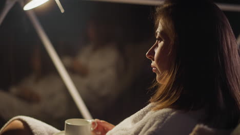 gloomy woman sits in armchair alone with thoughts. break from social life and enjoying being alone on holiday. lady reflects on pain at night in hotel room