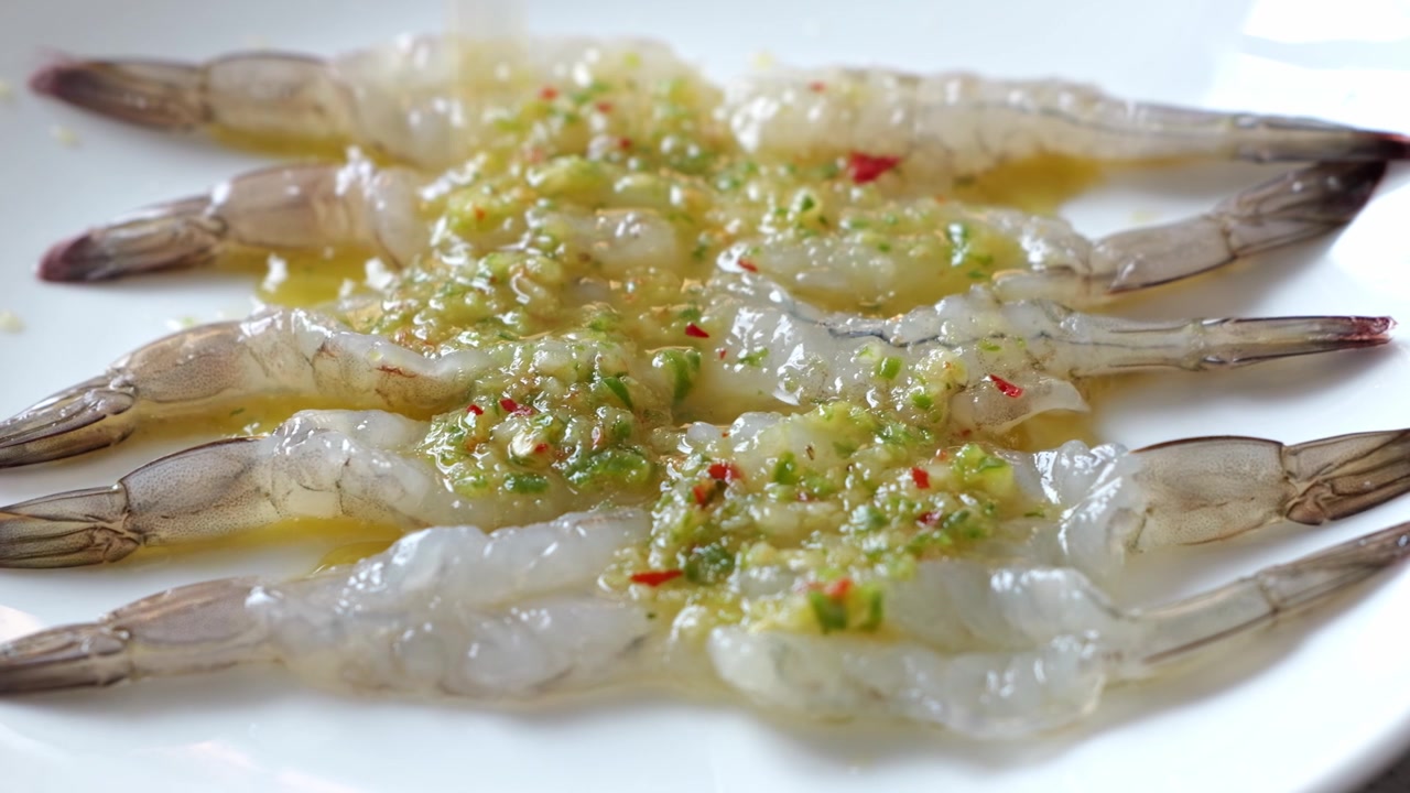 Tôm sống ướp tỏi, ớt và thảo mộc xanh trên đĩa trắng