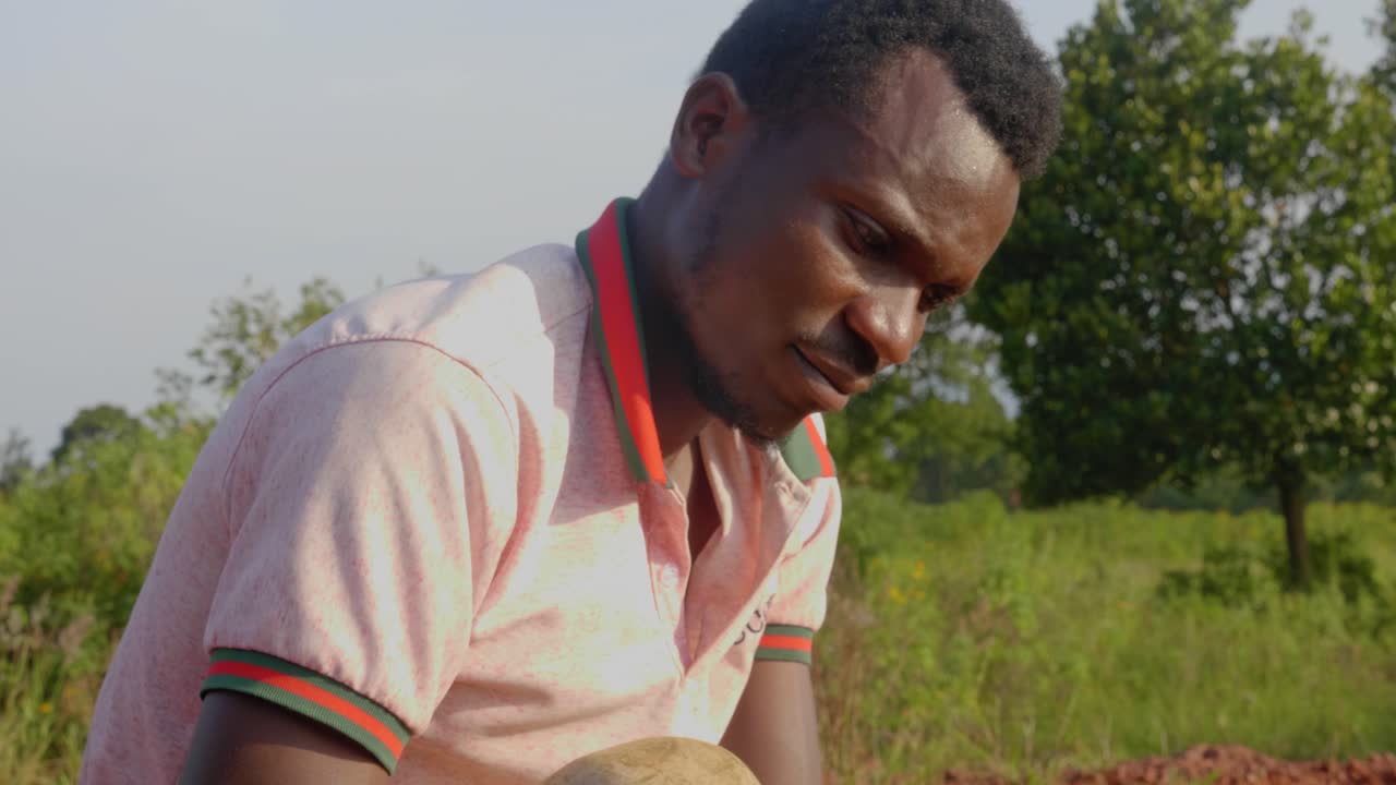 A close up shot of a young African mans face as he cooks meat over a fire in rural Africa