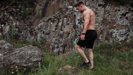 caucasian mid-aged strongman with naked torso walks up to a big stone. athlete makes an effort to lift or roll the rock.