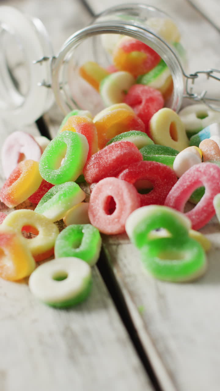 video vertical de caramelos de jalea derramándose de un frasco de vidrio sobre un fondo de madera