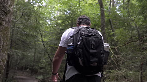 Man-walks-through-woods-with-backpack-in-southern-USA-lush-green-forest,-4K