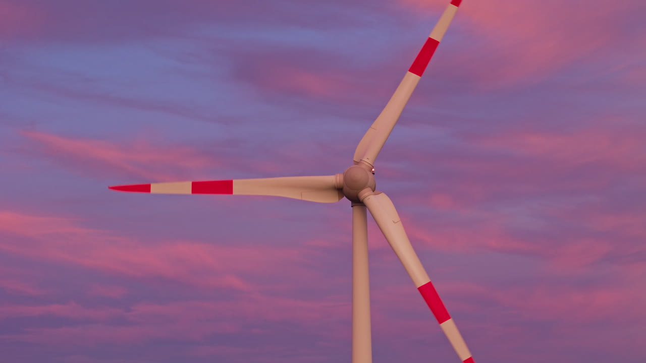 Una moderna turbina eolica si erge alta contro un cielo drammatico al tramonto, con la luce dell'ora d'oro che mostra