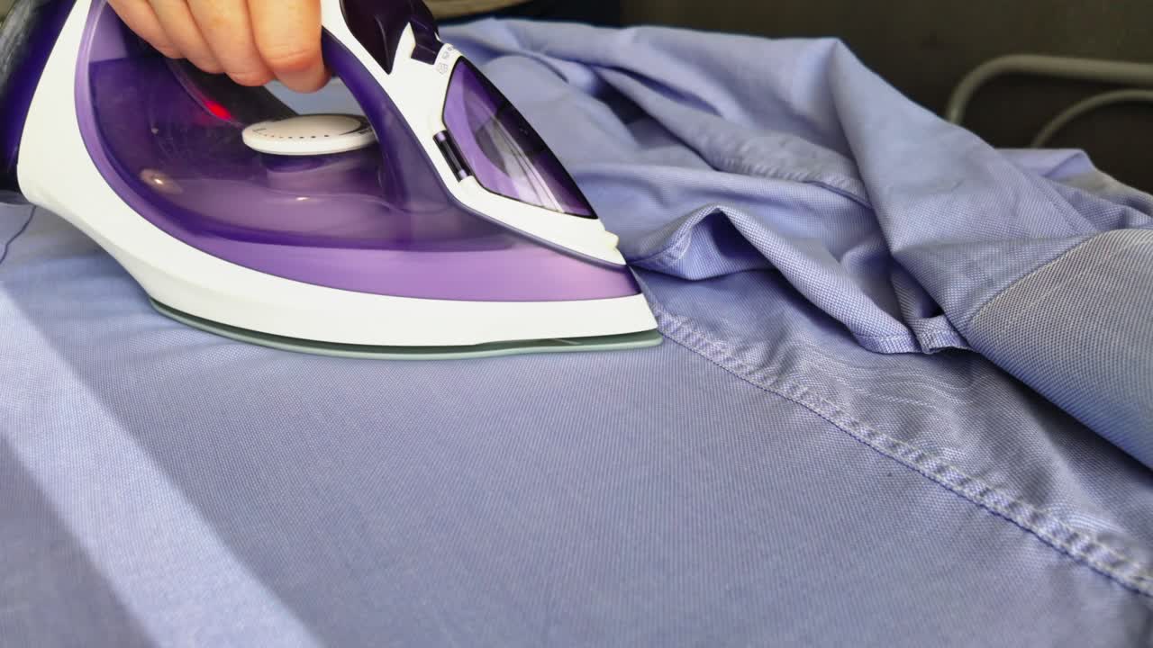 Hand Holding Electric Iron Ironing Clothes On an Ironing Board
