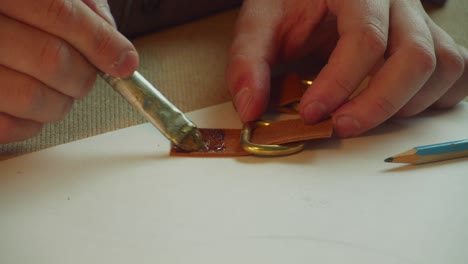 close-up of a tanner's hands painstakingly gluing together the fasteners of a women's leather bag with leather glue and a brush