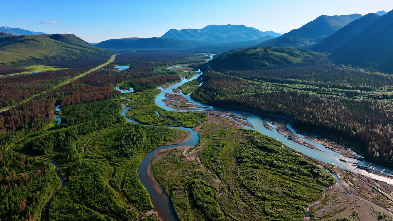 Footage above the green valley crossed by the narrow lines of the rivers. Beautiful mountains at backdrop. Alaska wilderness