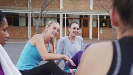 Diverse-female-basketball-team-sitting-on-ground-and-talking