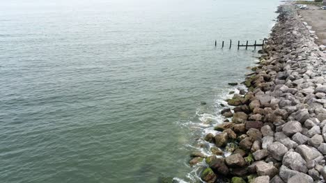 Aerial-view-above-splashing-ocean-tide-breaking-on-rocky-coastal-shoreline-pull-back-rising