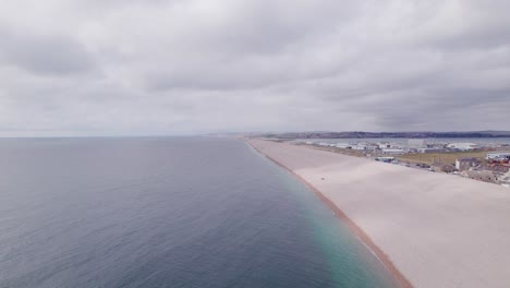 Disparo-De-Drones-Volando-Hacia-Atrás-A-Lo-Largo-De-La-Playa-De-Chesil-En-Un-Día-Soleado,-Weymouth,-Dorset,-Reino-Unido