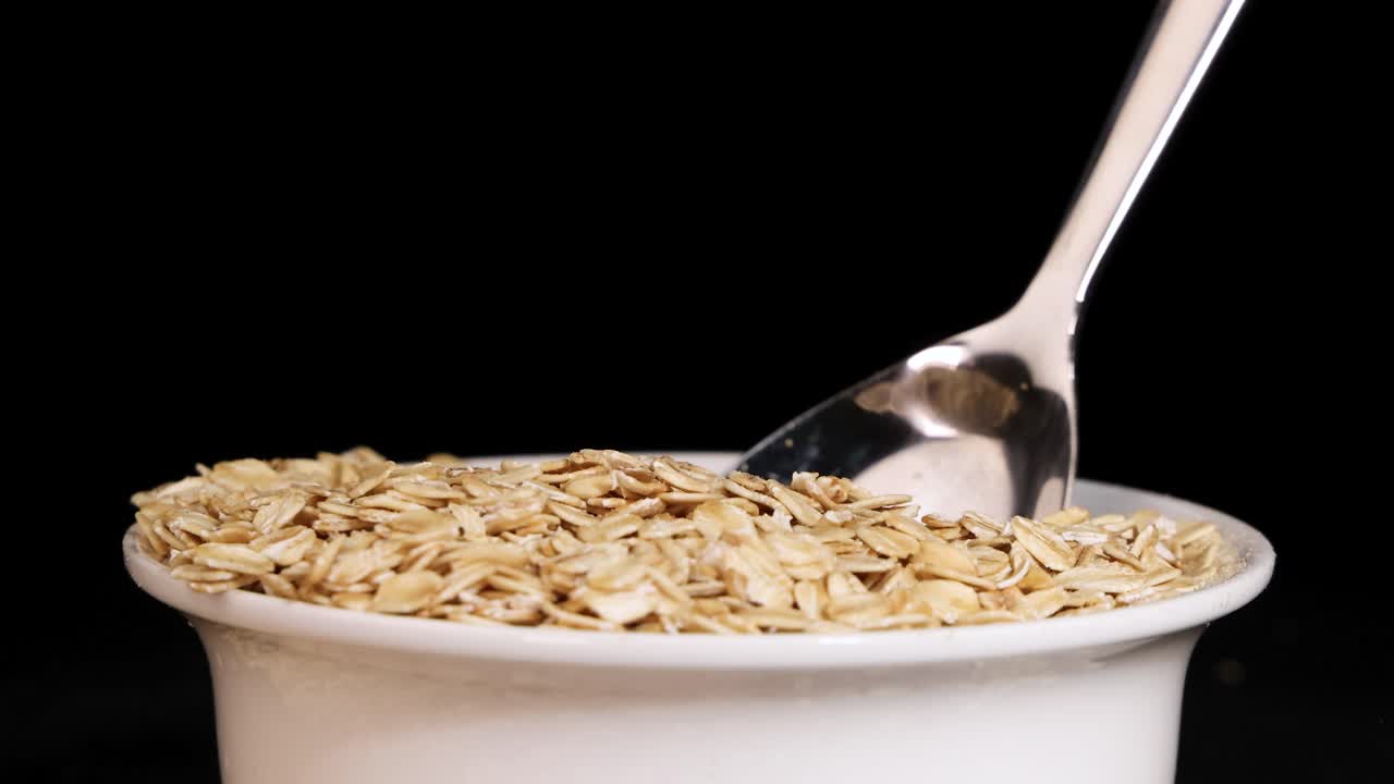 A spoon drops oats into a bowl against a black background, highlighting texture and motion in a 20-second sequence