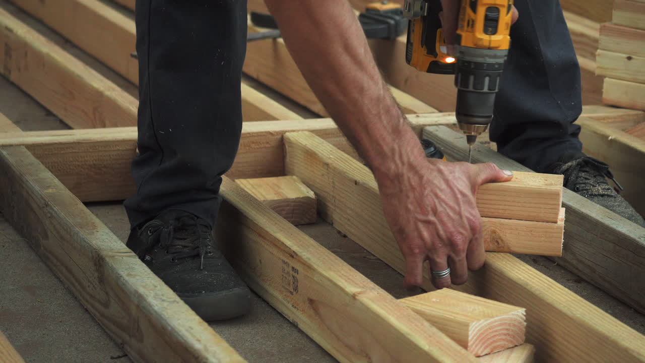 primer plano de un hombre perforando agujeros en bloques de madera con un taladro eléctrico, inseguro sin guantes