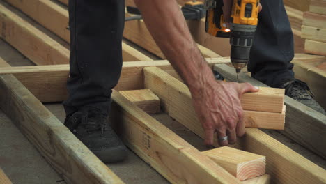 closeup of man drilling holes into wooden blocks with power drill, unsafe wearing no gloves