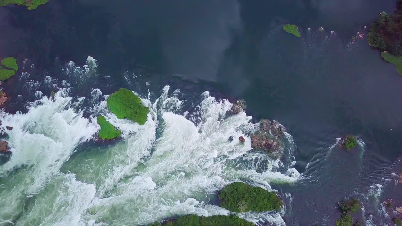 Aerial view of the rapids on the River Nile in Uganda, Africa, creating white water and foam and flowing around small islands covered with green vegetation, top down slow motion drone shot
