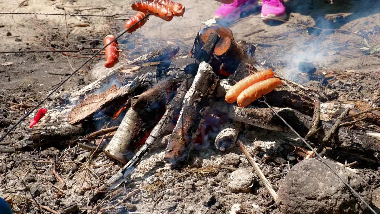 hornear salchichas en el fuego del campamento en un día soleado durante la temporada de campamento de verano