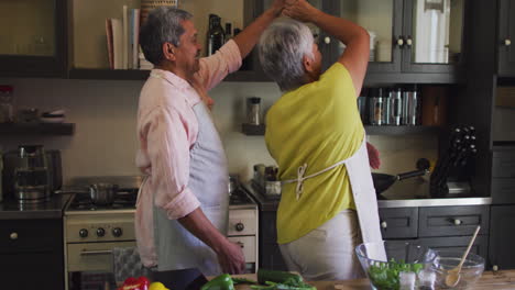 una feliz pareja biracial con delantales bailando en la cocina