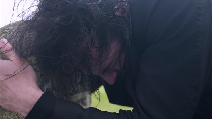 Distraught, emotional, crying man grieving the death of loved one in cemetery