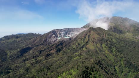 un primer plano aéreo del borde de un volcán humeante ijen con un lago turquesa y una montaña nublada en el fondo - java oriental, indonesia