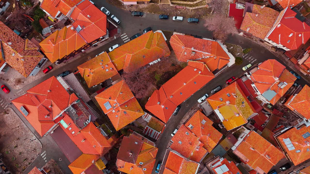 Top down aerial view of tiled roofs and streets. Orange tiled rooftops and narrow paved city streets
