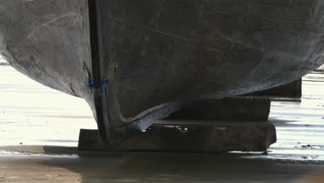 Forward-Bow-Of-Wooden-Boat-Being-Placed-Onto-Wooden-Blocks-On-Beach