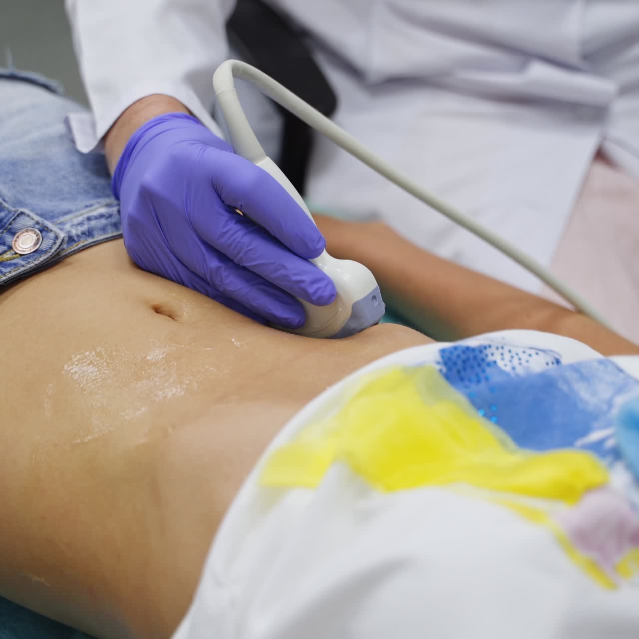 Unknown girl in t-shirt and jeans shorts lies on the doctor's couch. Physician moving the scanner by the patient's abdomen