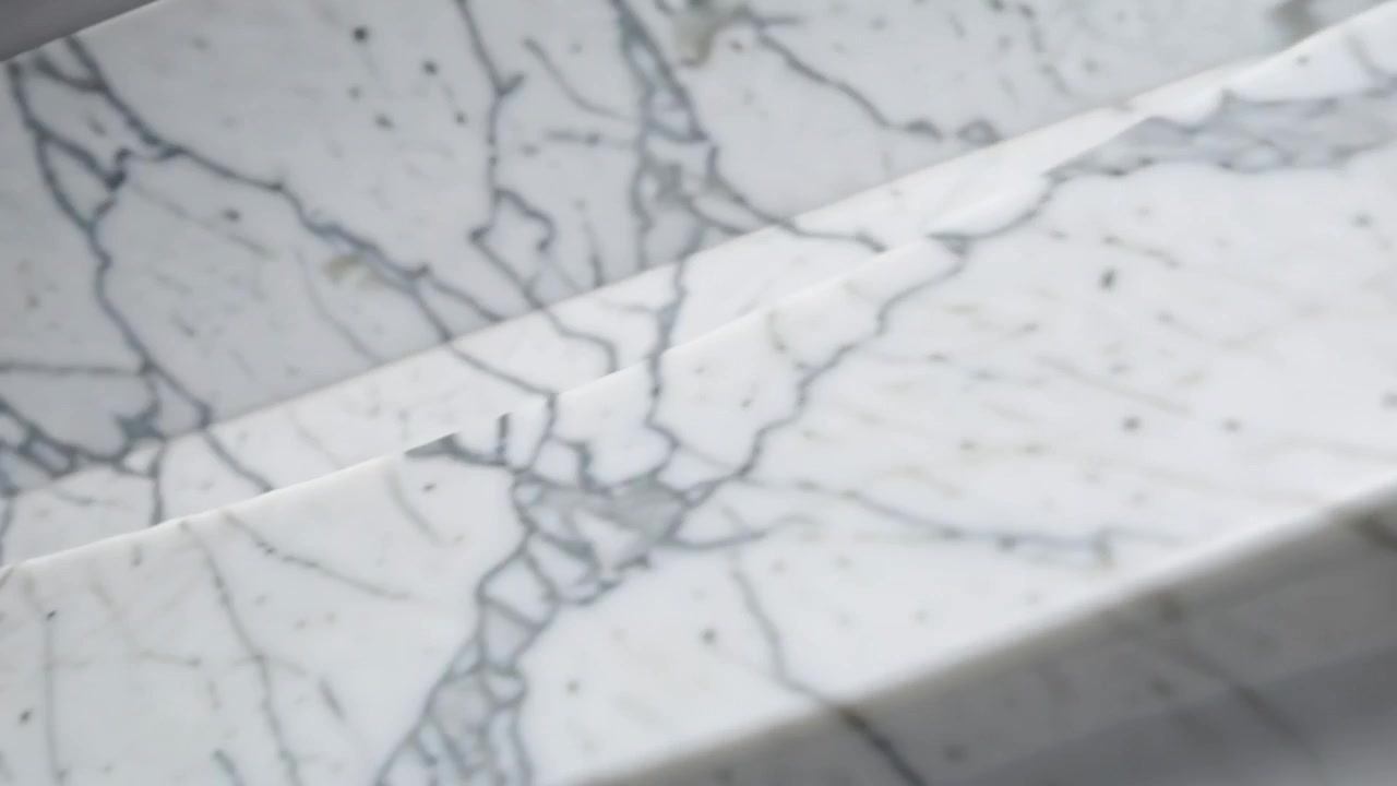 Telecamera che inizia una lenta panoramica su marmo lucido all'interno, rivelando un bordo scanalato e una sporgenza curva che mostra le venature.