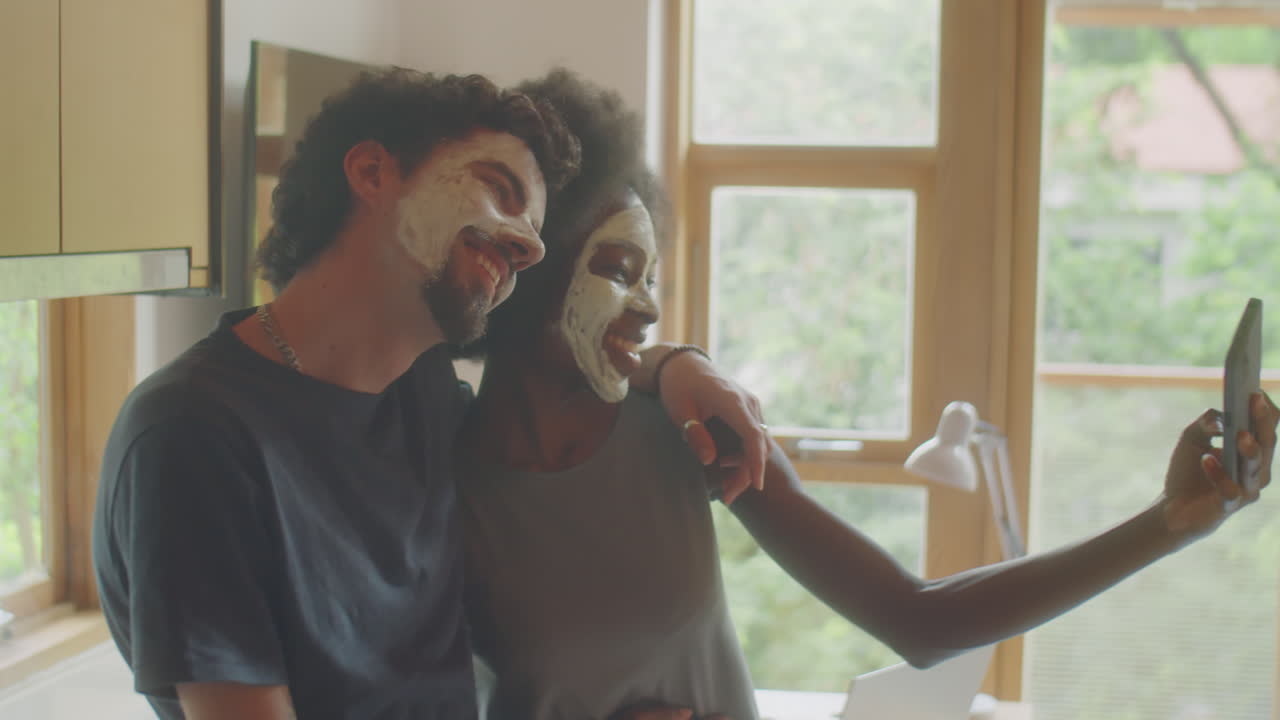 Cheerful Couple with Clay Masks Taking Selfie with Phone